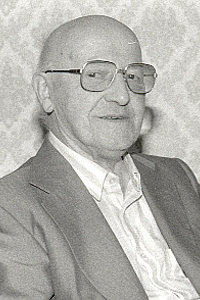 Ein älterer Mann mit Brille und Anzug lächelt in die Kamera.