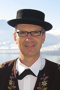 Ein Mann trägt traditionelle Kleidung und einen Hut vor einer schneebedeckten Landschaft.