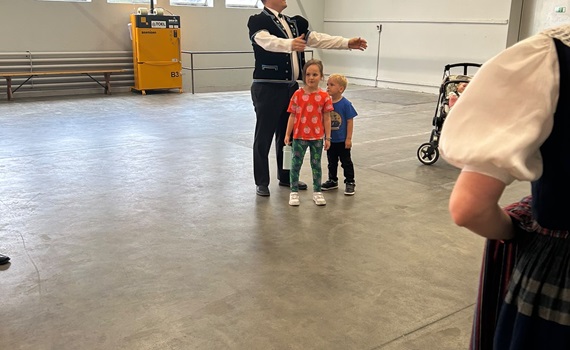 Ein Mann in traditioneller Kleidung steht vor zwei Kindern in einem großen Raum.