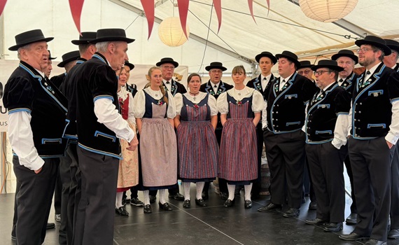Eine Gruppe von Menschen in traditioneller Tracht steht auf einer Bühne unter einem Zelt.