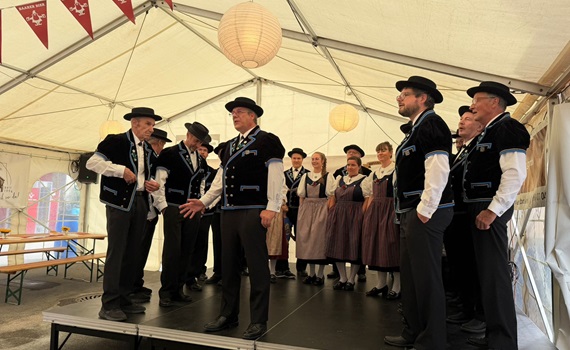 Eine Gruppe von Menschen in traditioneller Kleidung steht auf einer Bühne in einem Zelt.