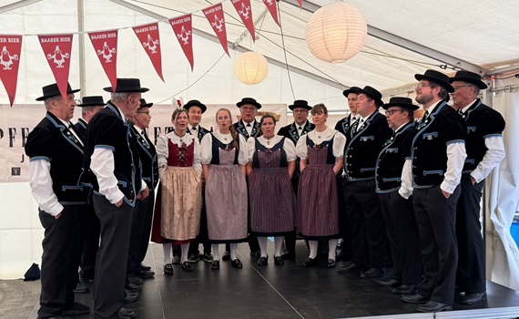 Eine Gruppe von Menschen in traditioneller Tracht steht auf einer Bühne unter einem Zelt.