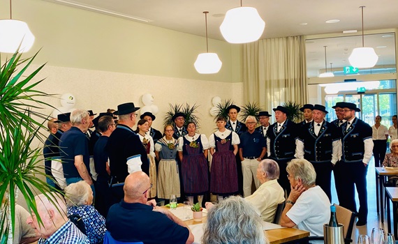 Eine Gruppe von Menschen in traditioneller Kleidung singt in einem Restaurant, während andere Gäste zuschauen.