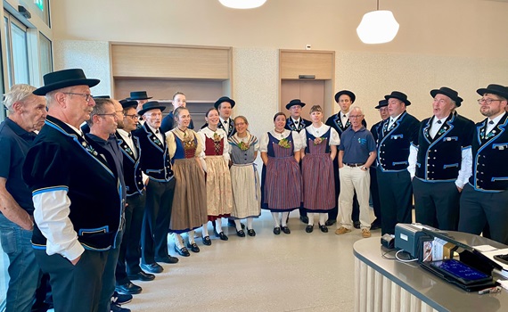Eine Gruppe von Menschen in traditioneller Kleidung steht in einem Raum und singt.