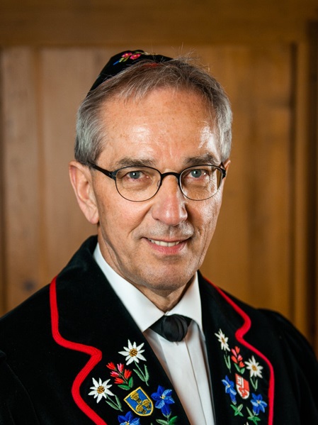 Ein Mann mit Brille trägt einen schwarzen, mit Blumen bestickten Anzug und ein weißes Hemd.